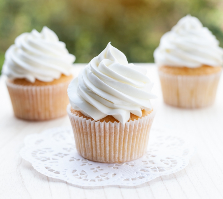 three cupcakes with white frosting on a white surface